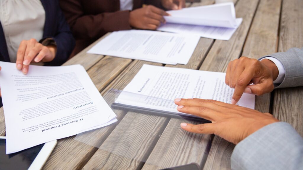 Pessoas de terno analisando documentos em uma mesa de madeira