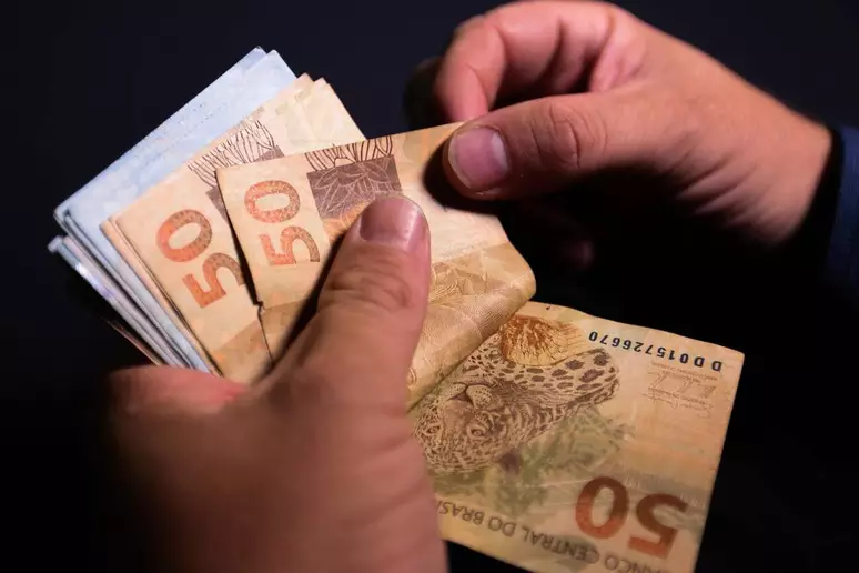 Mãos contando notas de dinheiro em reais