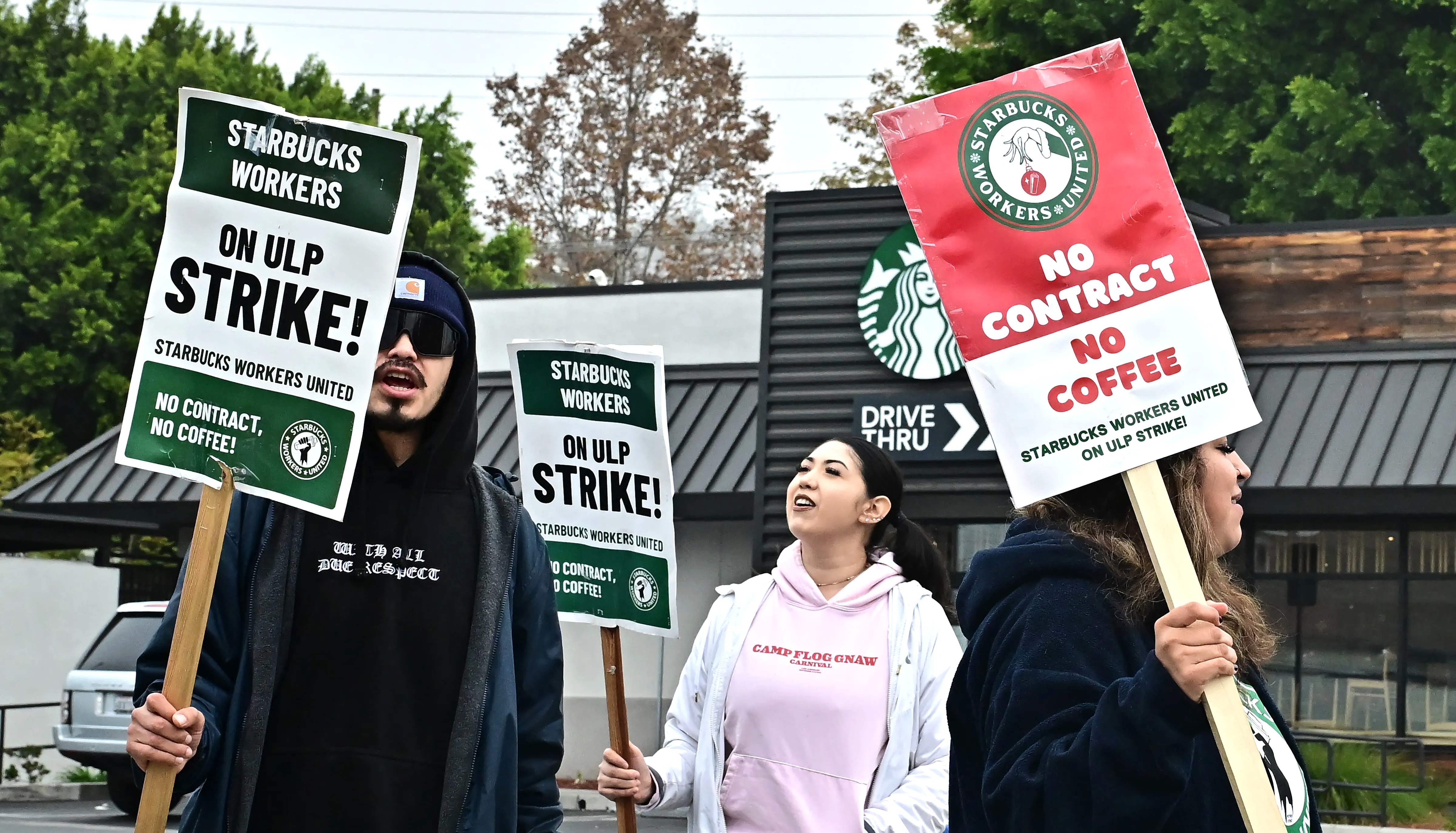 Trabalhadores com cartazes em inglês, estão de greve em frente ao Starbucks.